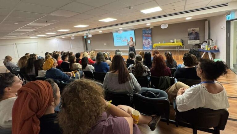 מרצה עומדת מול קהל נשים באולם ומעבירה הרצאה מעוררת השראה במסגרת פעילות הקומה הישראלית