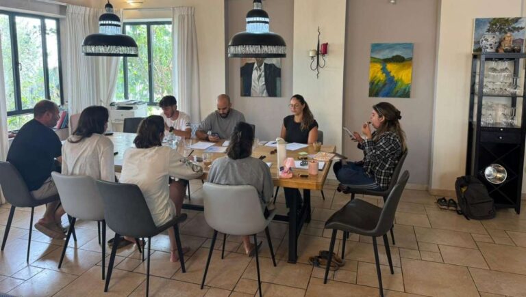 משתתפים יושבים סביב שולחן במפגש קבוצתי אינטימי העוסק בשיח, הקשבה וחשיבה משותפת במסגרת הקומה הישראלית