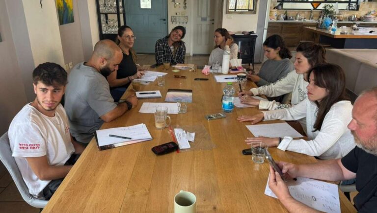 קבוצה יושבת סביב שולחן ומקיימת שיח וכתיבה במסגרת מפגש למידה וחשיבה של הקומה הישראלית